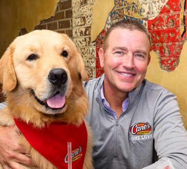 Kirk Herbstreit sits in a booth with his golden retriever Peter, who wears a red Raising Cane's bandana.