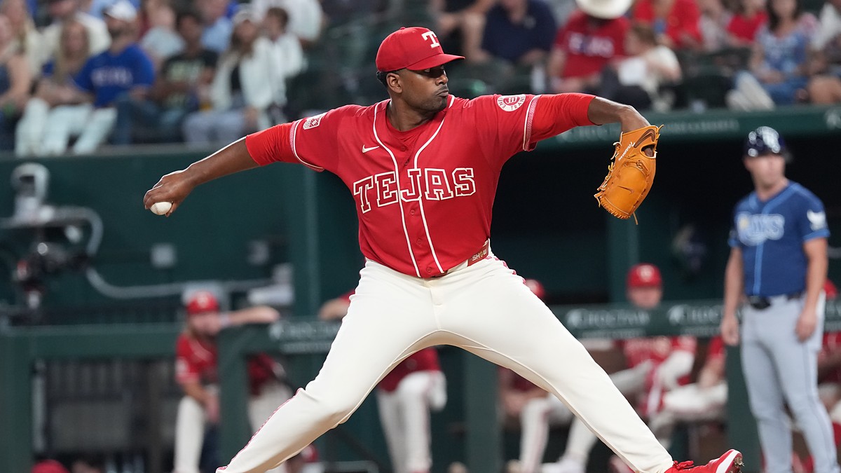 Texas Rangers right-hander Kumar Rocker, No. 80, strides toward the plate in a red Tejas jersey.
