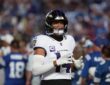 Baltimore Ravens safety Kyle Hamilton walks onto the field adjusting his gloves in a white Ravens road jersey.