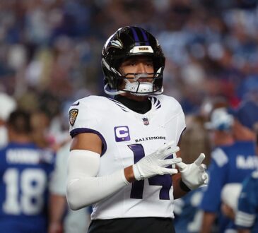 Baltimore Ravens safety Kyle Hamilton walks onto the field adjusting his gloves in a white Ravens road jersey.