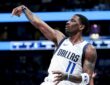 Dallas Mavericks guard Kyrie Irving holds his follow-through after a shot in a white Dallas jersey.