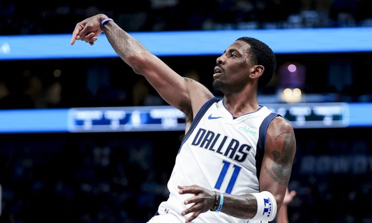 Dallas Mavericks guard Kyrie Irving holds his follow-through after a shot in a white Dallas jersey.