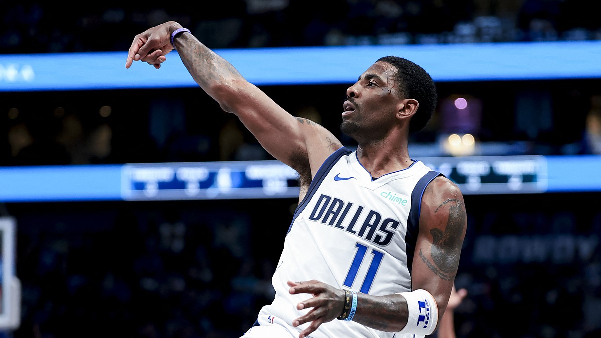 Dallas Mavericks guard Kyrie Irving holds his follow-through after a shot in a white Dallas jersey.