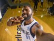 Dallas Mavericks guard Kyrie Irving grins while holding the camera at arm's length for a selfie on a gym floor.