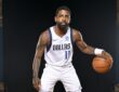 Dallas Mavericks guard Kyrie Irving crouches in a dribbling stance with a basketball against a black backdrop.