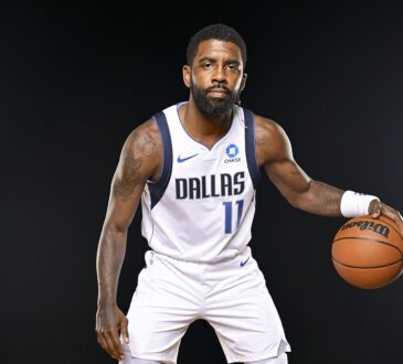 Dallas Mavericks guard Kyrie Irving crouches in a dribbling stance with a basketball against a black backdrop.