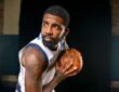 Dallas Mavericks guard Kyrie Irving holds a basketball near his shoulder and looks off to the side during a photo shoot.