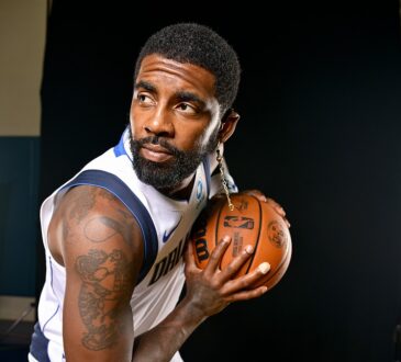 Dallas Mavericks guard Kyrie Irving holds a basketball near his shoulder and looks off to the side during a photo shoot.