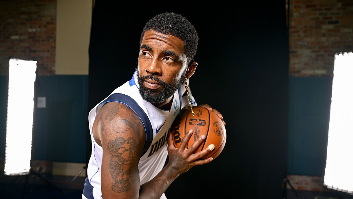 Dallas Mavericks guard Kyrie Irving holds a basketball near his shoulder and looks off to the side during a photo shoot.