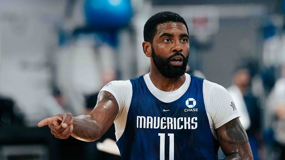 Dallas Mavericks guard Kyrie Irving points to his right while wearing a blue No. 11 practice jersey over a white shirt.