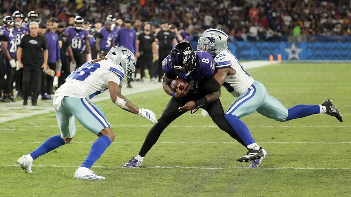 Cowboys safety Caleb Downs wraps up Ravens quarterback Lamar Jackson as cornerback Shavon Revel Jr. closes in near the sideline.