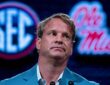 Lane Kiffin sits in front of SEC and Ole Miss logos while speaking at SEC media days.