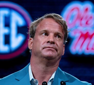 Lane Kiffin sits in front of SEC and Ole Miss logos while speaking at SEC media days.