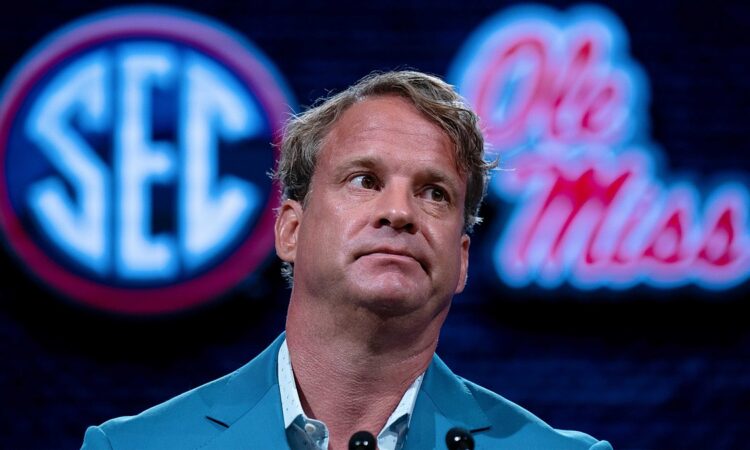 Lane Kiffin sits in front of SEC and Ole Miss logos while speaking at SEC media days.
