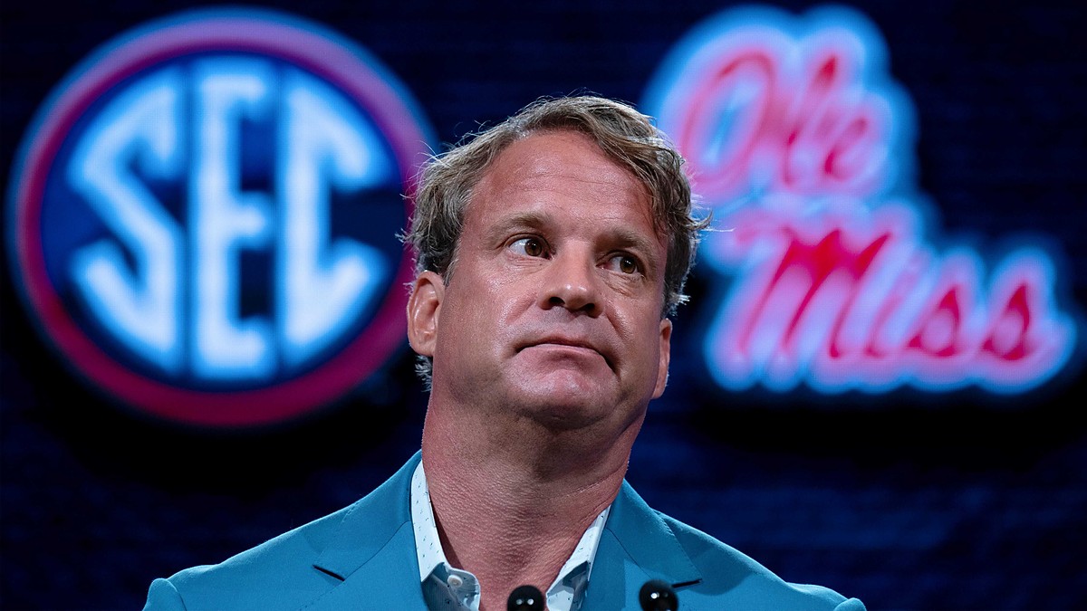 Lane Kiffin sits in front of SEC and Ole Miss logos while speaking at SEC media days.