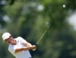 Golfer Lindy Duncan follows through on an iron shot as the ball flies against a backdrop of blurred trees.