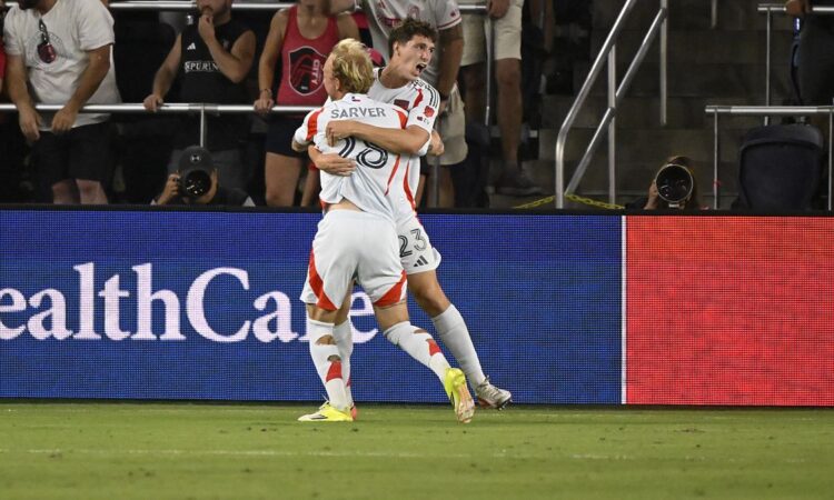 FC Dallas forward Logan Farrington is lifted by a teammate while celebrating a goal in front of St. Louis supporters.