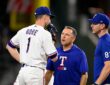 Rangers starting pitcher MacKenzie Gore stands on the mound talking with two members of the coaching and training staff.