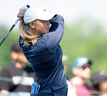 Golfer Maja Stark finishes her swing with the club wrapped behind her head as spectators watch.