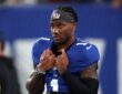 New York Giants wide receiver Malik Nabers, wearing a Giants headband, grips the collar of his jersey on the field.