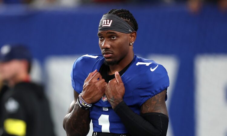 New York Giants wide receiver Malik Nabers, wearing a Giants headband, grips the collar of his jersey on the field.