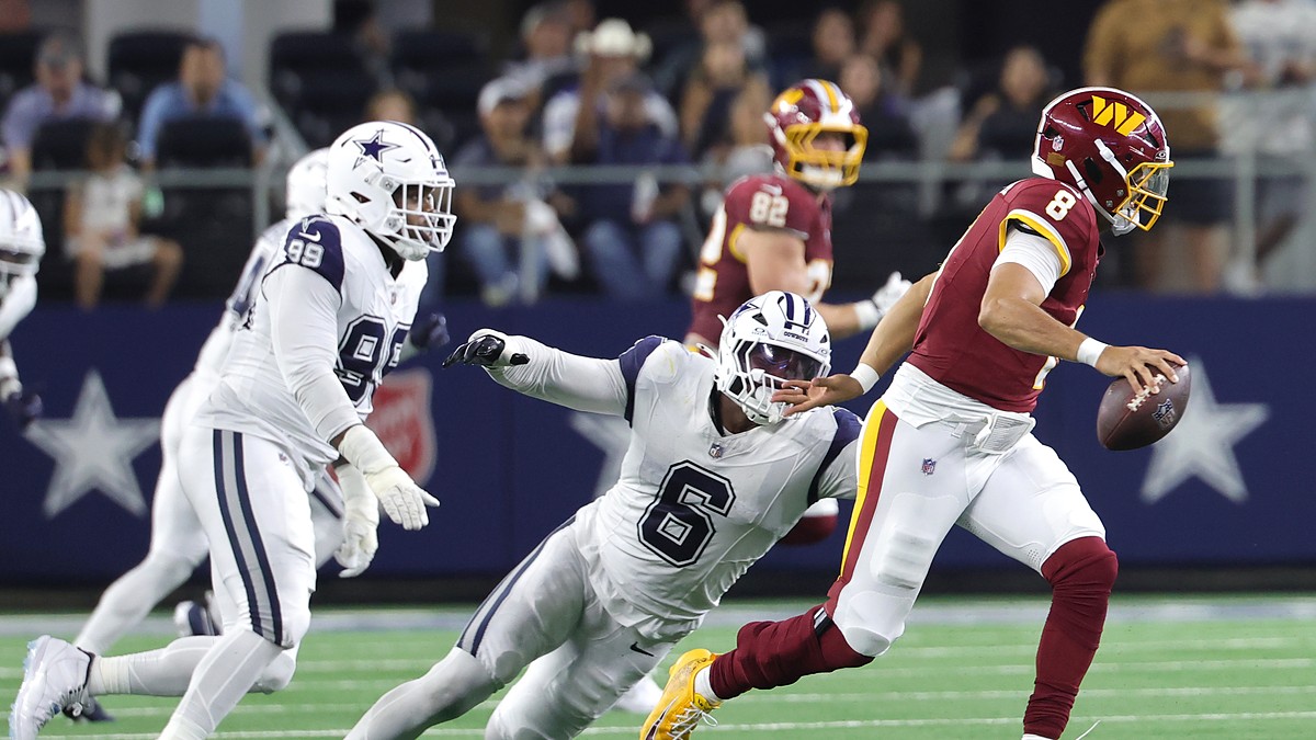 Washington Commanders quarterback Marcus Mariota scrambles as Cowboys linebacker Donovan Ezeiruaku dives after him.