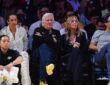 Mark Walter sits with his arms crossed next to Jeanie Buss in courtside seats at a Lakers game.
