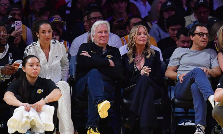 Mark Walter sits with his arms crossed next to Jeanie Buss in courtside seats at a Lakers game.