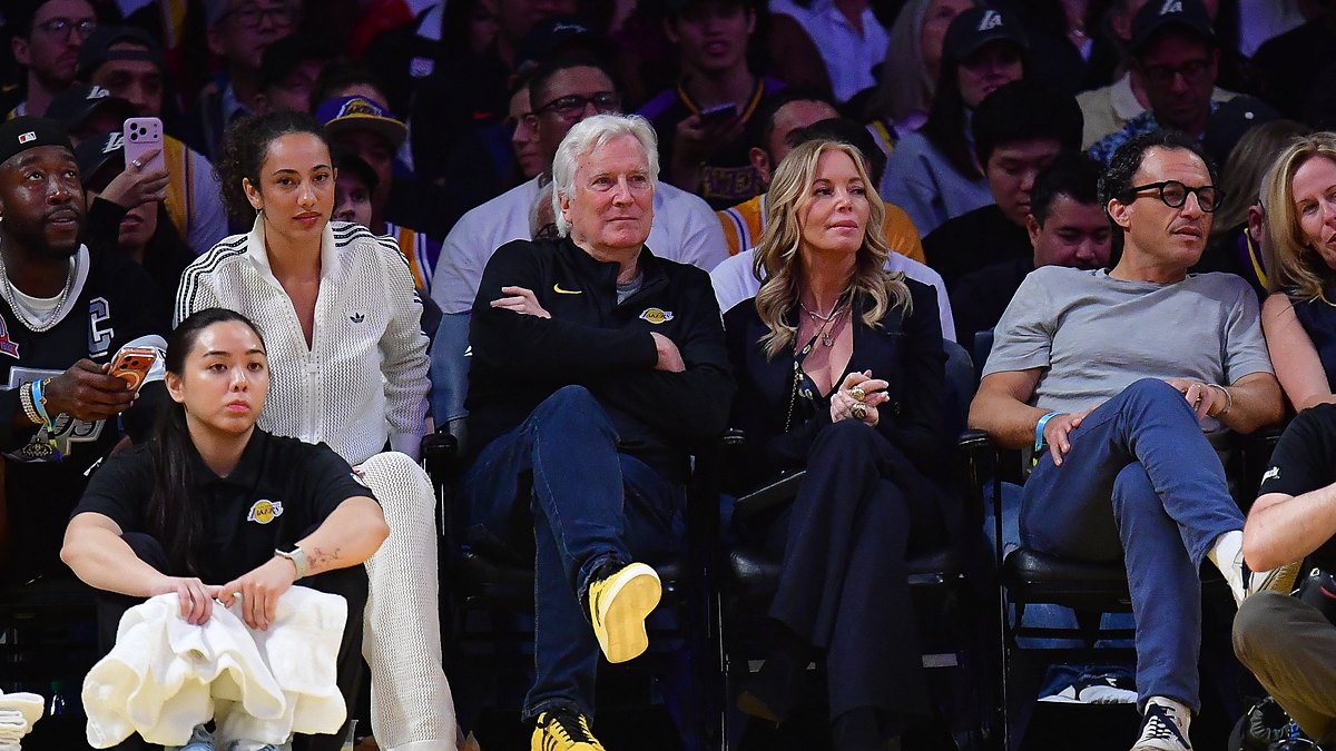 Mark Walter sits with his arms crossed next to Jeanie Buss in courtside seats at a Lakers game.