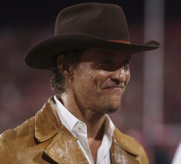 Actor Matthew McConaughey stands on the sideline in a brown hat and leather jacket before a Texas game.