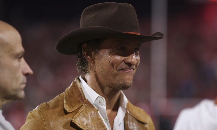 Actor Matthew McConaughey stands on the sideline in a brown hat and leather jacket before a Texas game.