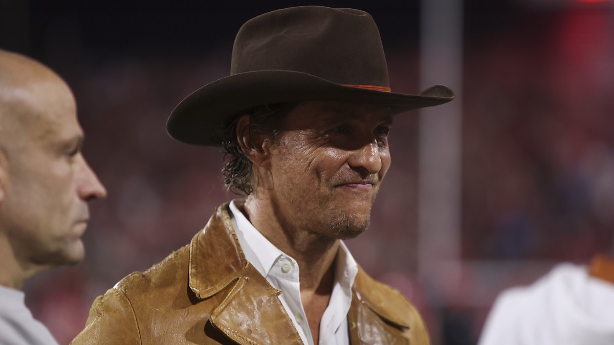 Actor Matthew McConaughey stands on the sideline in a brown hat and leather jacket before a Texas game.