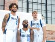 Dallas Mavericks center Dereck Lively II, guard Kyrie Irving, and forward Cooper Flagg pose together in a brick gym.