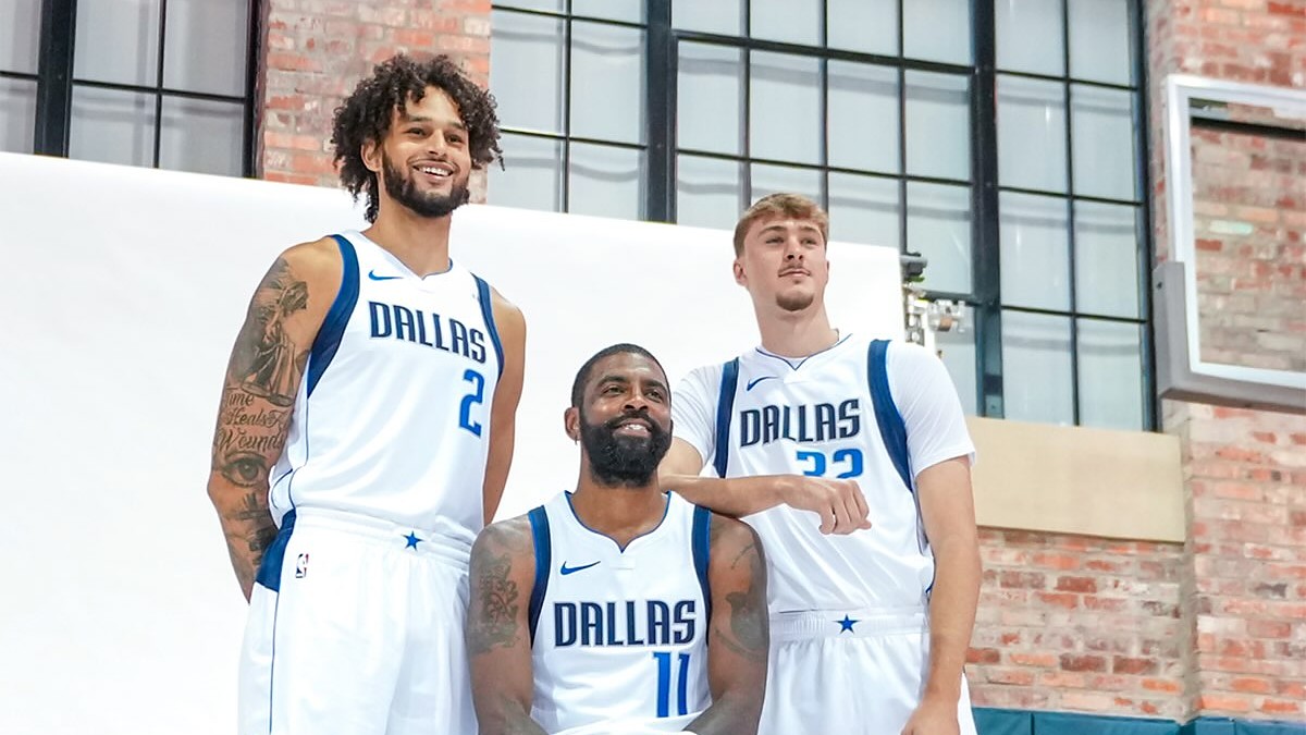 Dallas Mavericks center Dereck Lively II, guard Kyrie Irving, and forward Cooper Flagg pose together in a brick gym.