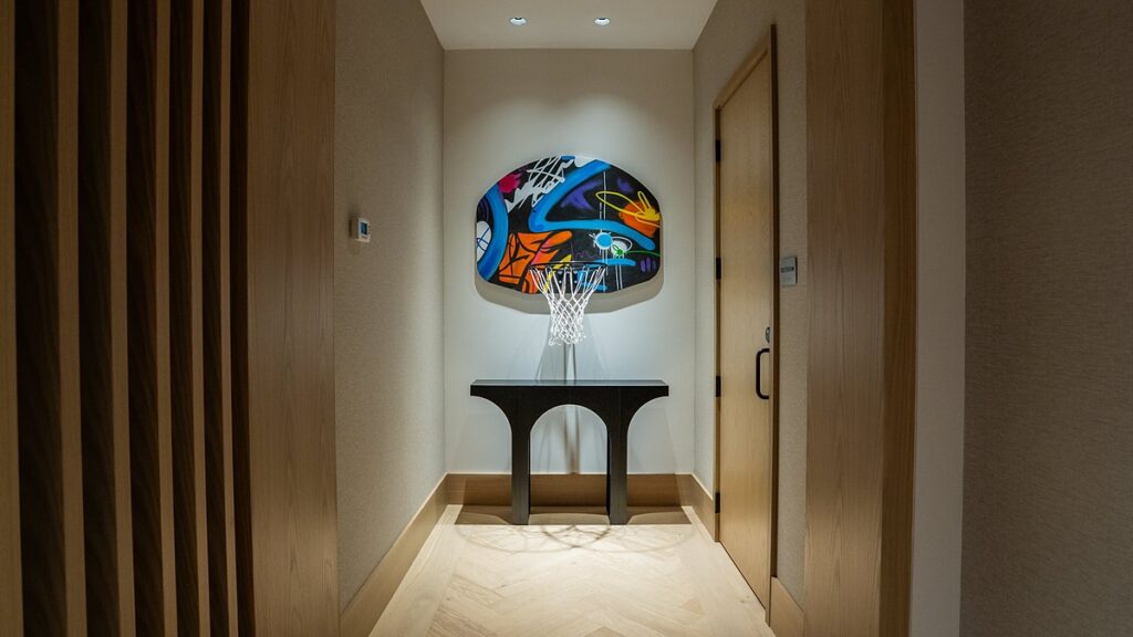 Dallas Mavericks practice facility hallway with a graffiti-painted backboard and hoop mounted above a black console table.