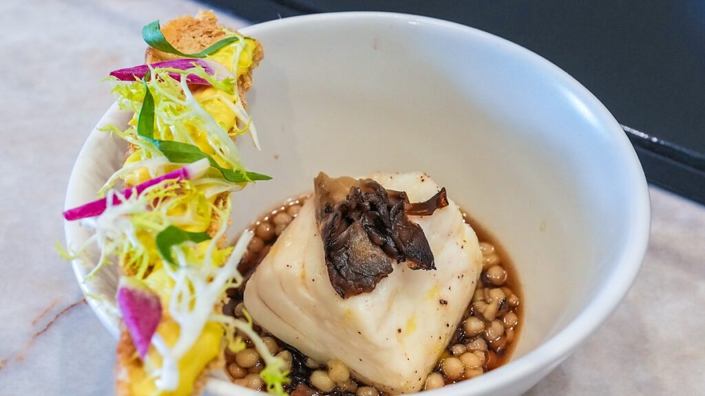 Dallas Mavericks Champions Performance Kitchen fish fillet topped with mushrooms in a bowl with a garnished toast.