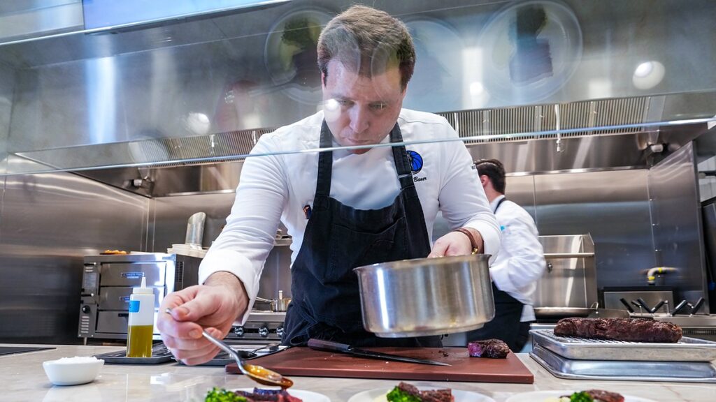 Dallas Mavericks culinary director John Bauer spoons sauce onto plated steak in the practice facility kitchen.