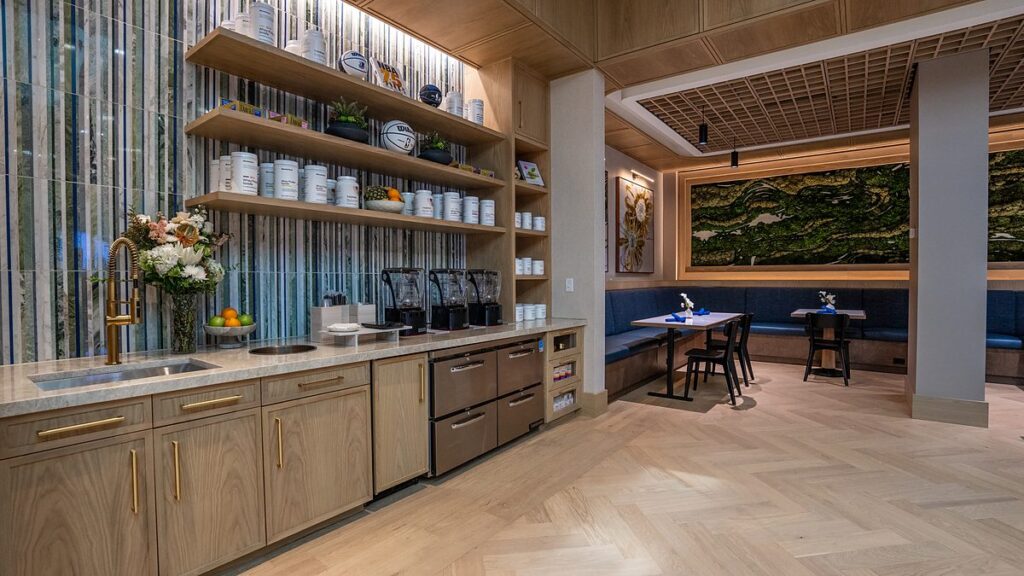 Dallas Mavericks practice facility dining room service counter with open shelves, blenders, and a moss mural beyond.