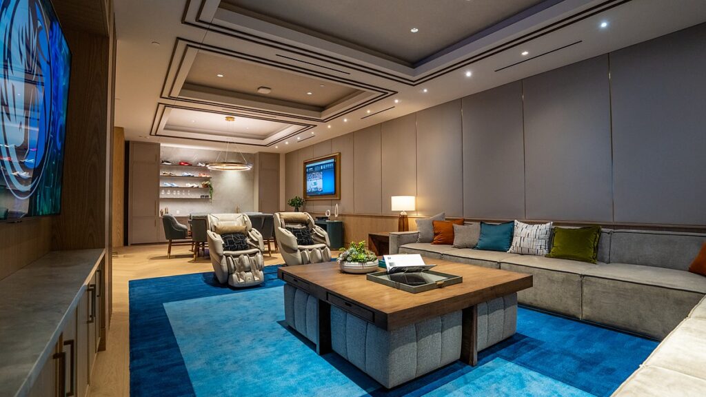 Dallas Mavericks players’ lounge with a large coffee table on a blue rug, a sectional sofa, and massage chairs.