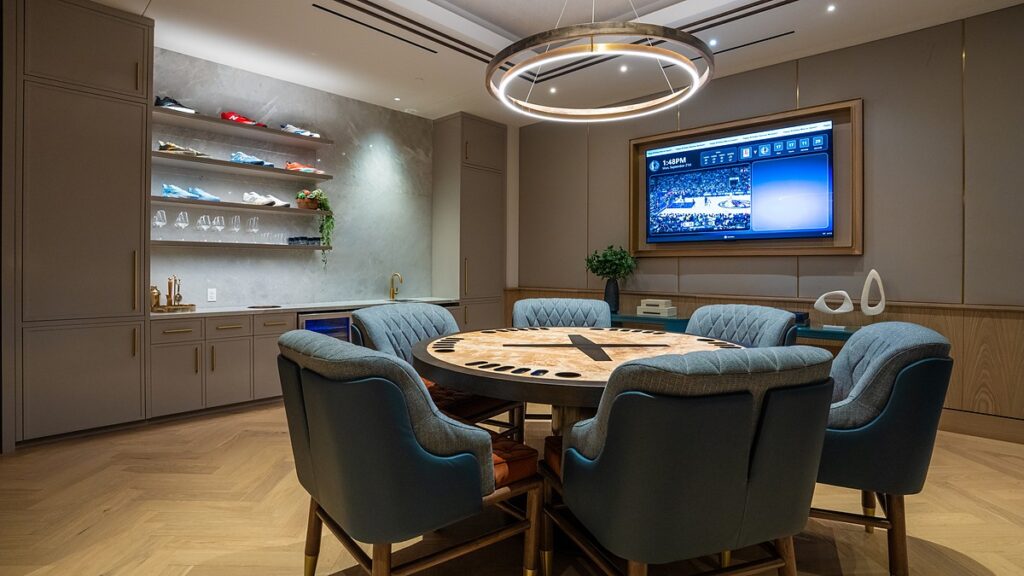 Dallas Mavericks players’ lounge card table with blue chairs, a sneaker display on lighted shelves, and a wall-mounted TV.