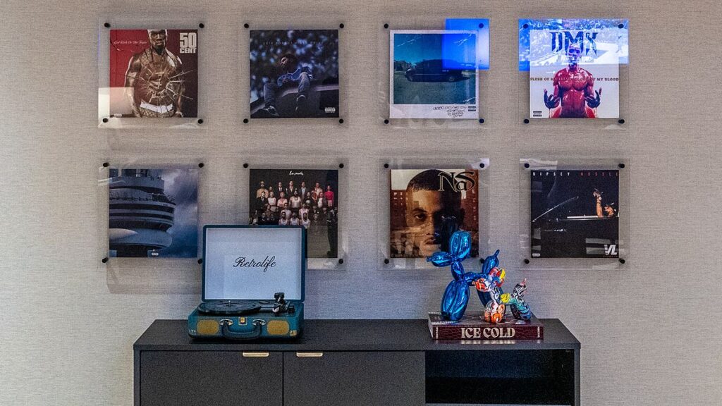 Dallas Mavericks players’ lounge wall of framed hip-hop album covers above a cabinet with a turntable and a blue balloon dog sculpture.