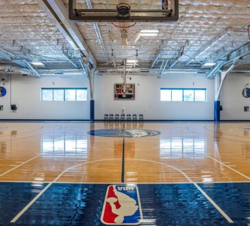 Dallas Mavericks practice court viewed from under a basket, with the NBA logo painted along the baseline.