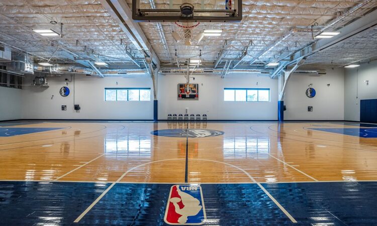 Dallas Mavericks practice court viewed from under a basket, with the NBA logo painted along the baseline.