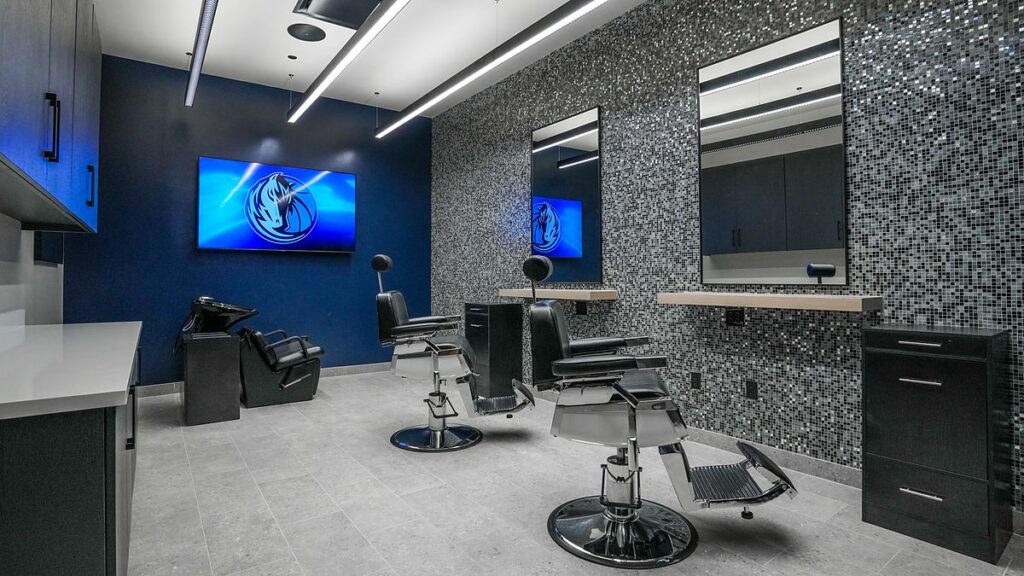 Dallas Mavericks team barbershop with two barber chairs, mirrors, a shampoo station, and a TV showing the Mavericks logo.