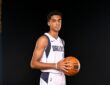 Dallas Mavericks guard Max Christie holds a basketball at his side in a white Dallas jersey against a black backdrop.