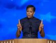 Former first lady Michelle Obama gestures with both index fingers raised while speaking at a podium.