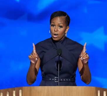 Former first lady Michelle Obama gestures with both index fingers raised while speaking at a podium.