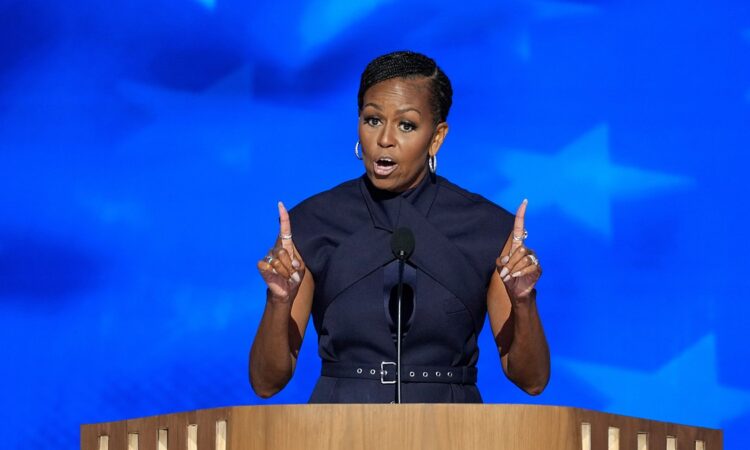 Former first lady Michelle Obama gestures with both index fingers raised while speaking at a podium.