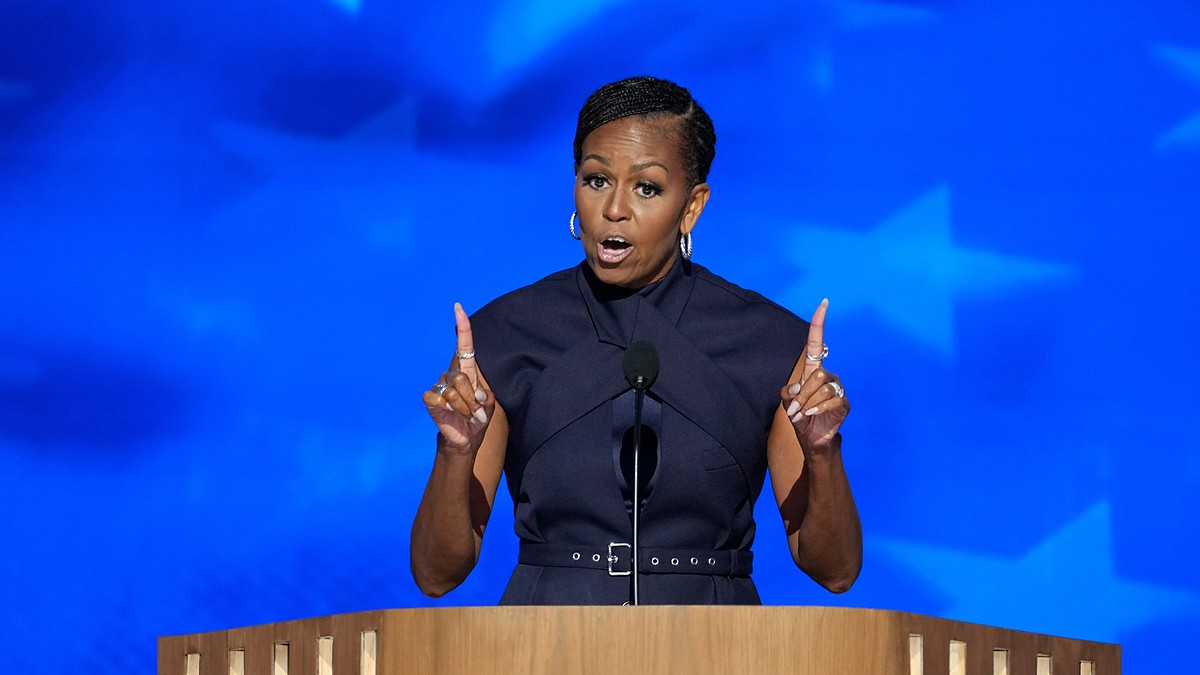 Former first lady Michelle Obama gestures with both index fingers raised while speaking at a podium.