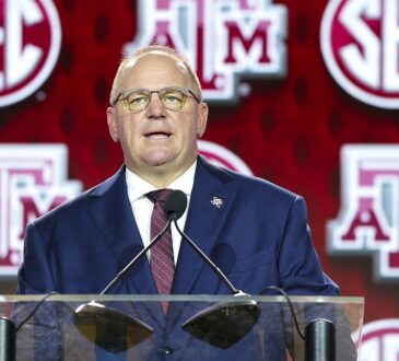 Texas A&M head coach Mike Elko speaks at a podium in front of an SEC and Aggies backdrop during media days.